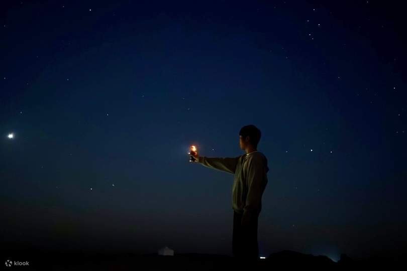 A silhouette holding a small light under a star-filled sky — a quiet moment in the night.